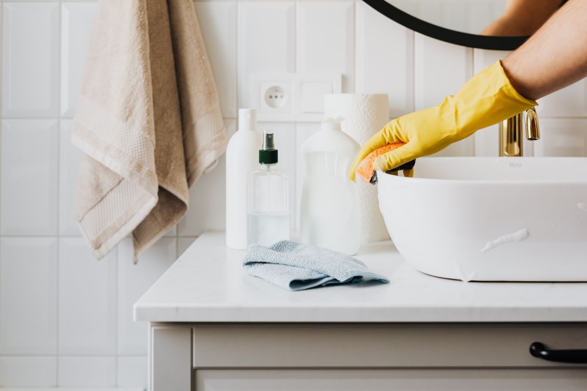 Limpeza de um lavatório com esponja e luvas de proteção